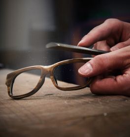 A person wearing glasses carefully fixes a pair of wooden glasses, highlighting attention to detail in the repair process.